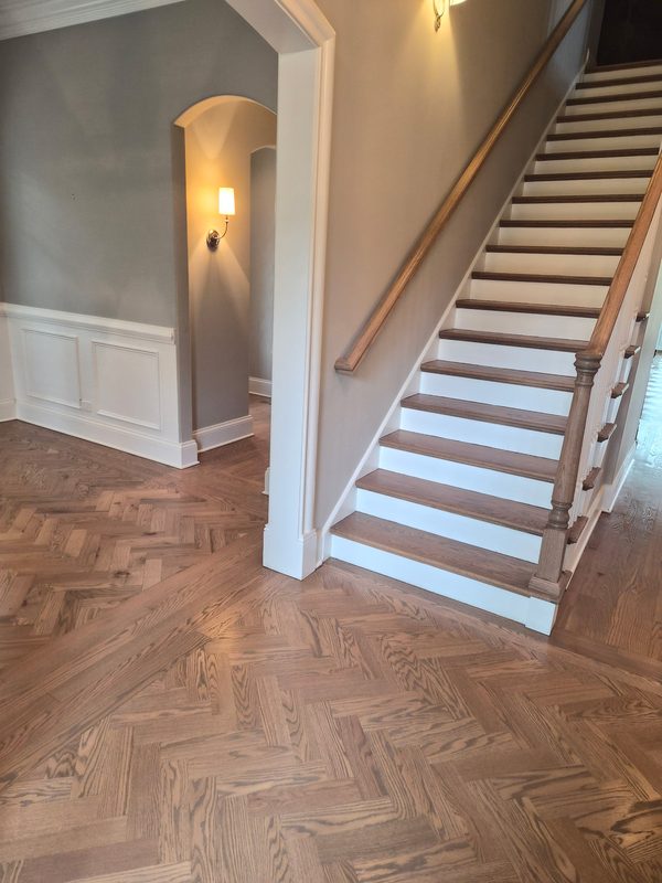 Herringbone hardwood floor and matching stained stair treads with white risers in a two-story entry