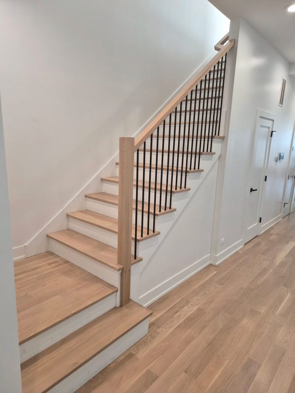 White oak stair treads with black iron balusters matching the hallway hardwood floor